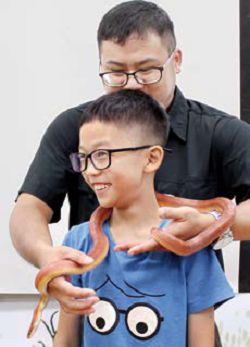 新北市立圖書館三峽分館透過講師引導，讓孩子體驗把蛇圍在脖子上。