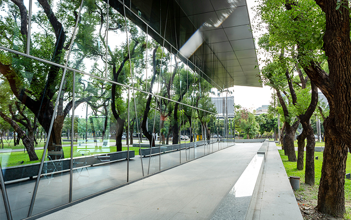 屏東總圖為保留入口的老樟樹，建築設計以鏡面玻璃與挑高空間延伸視覺，讓綠色地景得以延續。