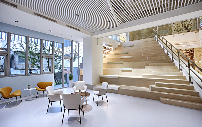 許良宇圖書館建築外觀與周邊山景自然融合，將戶外的綠意景觀一路延續至室內。館內以純淨的白色為主色調，搭配溫暖色塊點綴，透過大面積玻璃窗引入自然光線，營造出開闊、明亮的閱讀氛圍。