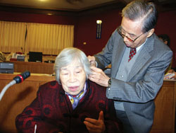 2005年12月，琦君參加琦君研究中心成立茶會，先生李唐基為她掛上助聽器。