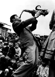 《賣藝者》周鑫泉，1968。仰角度抓住了賣藝者姿態聚焦神態，延伸觀眾好奇者聚精會神視線，去強調誇張與稍微變形，創意人物之間互動的瞬間。