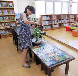 館員謝淑貞把剛進的宮崎駿全套作品擺開，準備拍照放上臉書宣傳。其實一樓圖書室這張木桌大有來頭。